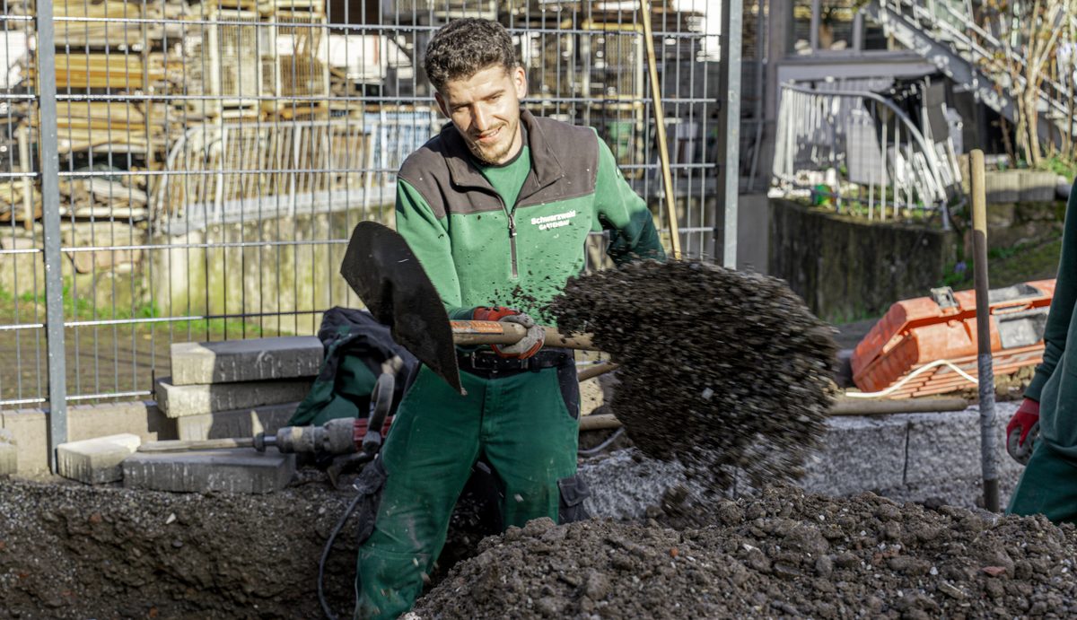 Mitarbeiter wirft mit der Schaufel Erde auf einer Baustelle auf