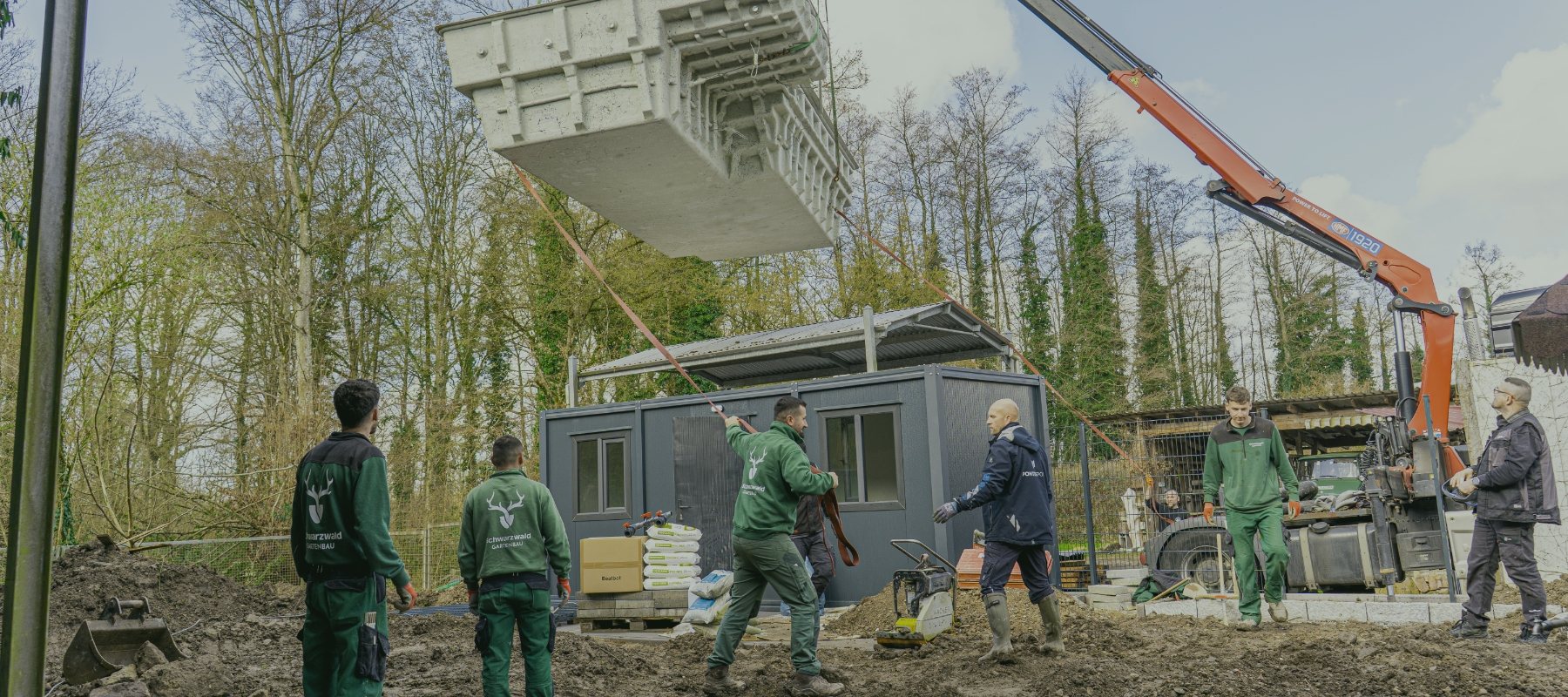 Team setzt mit einem Kran einen Baucontainer auf einem Grundstück ab