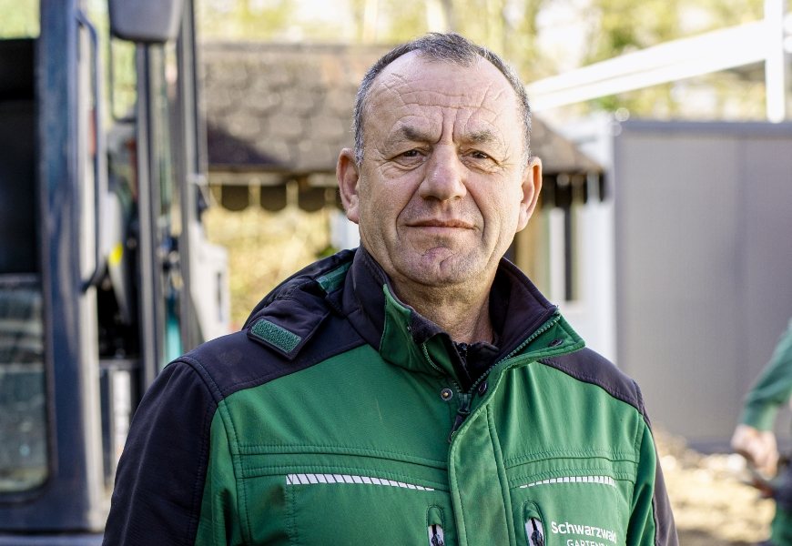 Porträt eines Mitarbeiters im Firmen-T-Shirt vor herbstlichem Laub