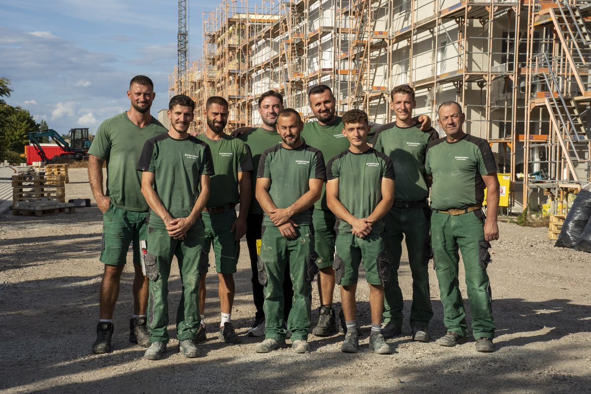 Das Team von Schwarzwald Gartenbau in grüner Arbeitskleidung vor einem eingerüsteten Neubau