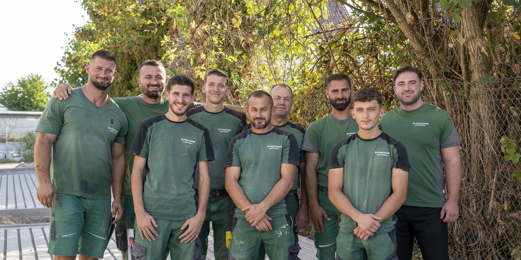 Neun Mitarbeiter von Schwarzwald Gartenbau nebeneinander vor einer bewachsenen Wand