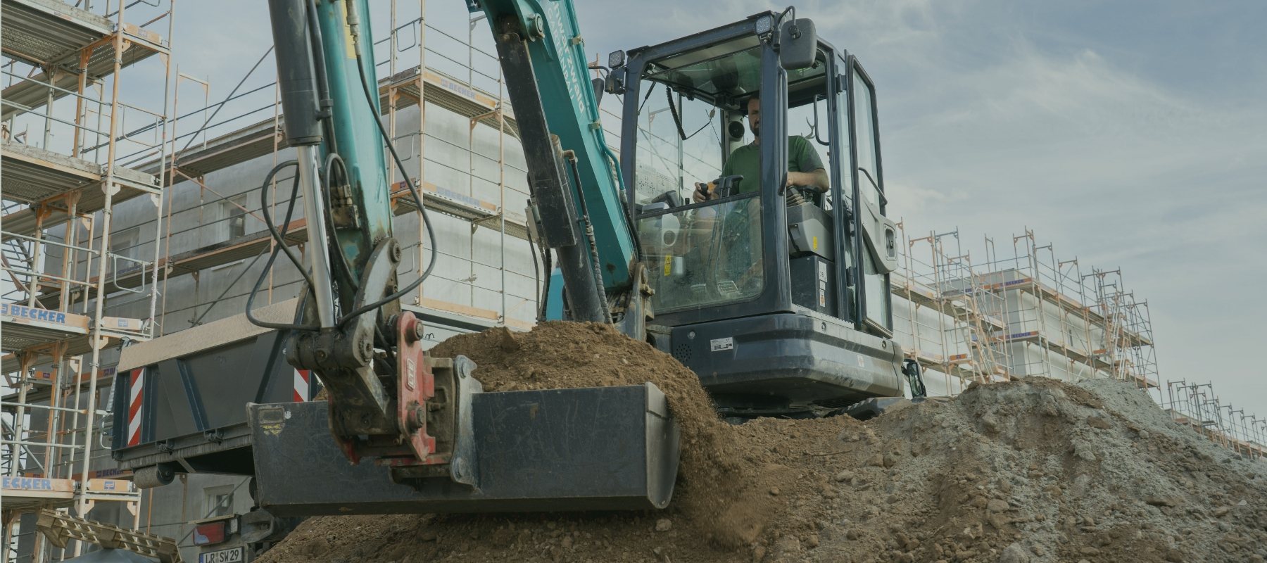 Bagger hebt Erde aus und lädt sie neben einem eingerüsteten Gebäude auf