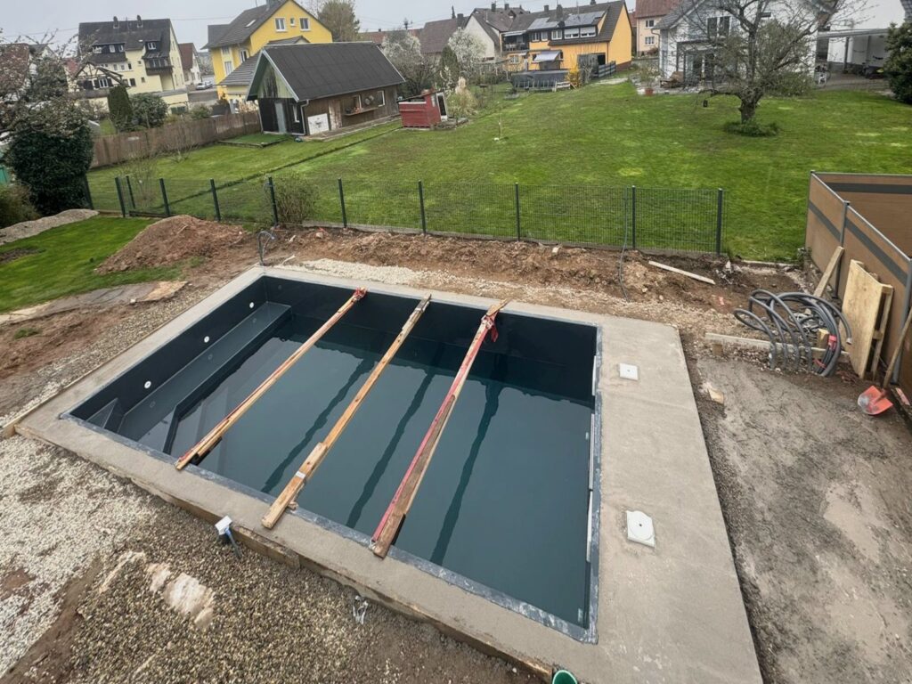 Vorher: Baustelle: eingesetztes Poolbecken mit Abdeckbrettern, ringsum noch offener Boden