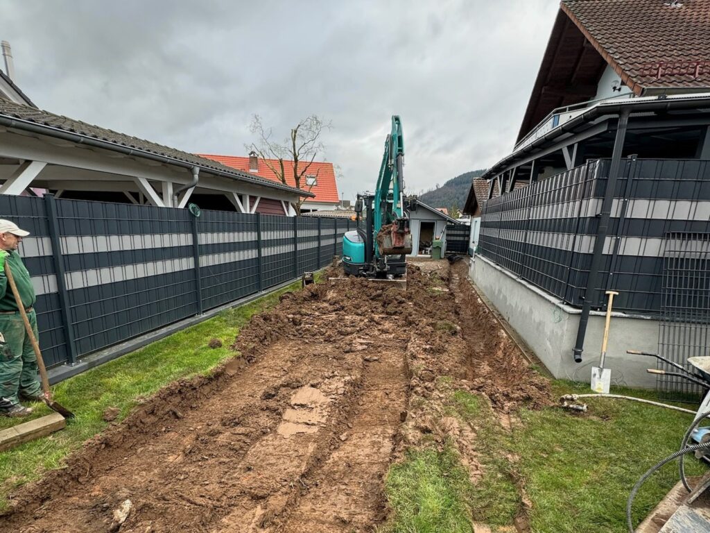 Vorher: Schmaler Garten mit frischem Aushub und Minibagger zwischen zwei Zäunen